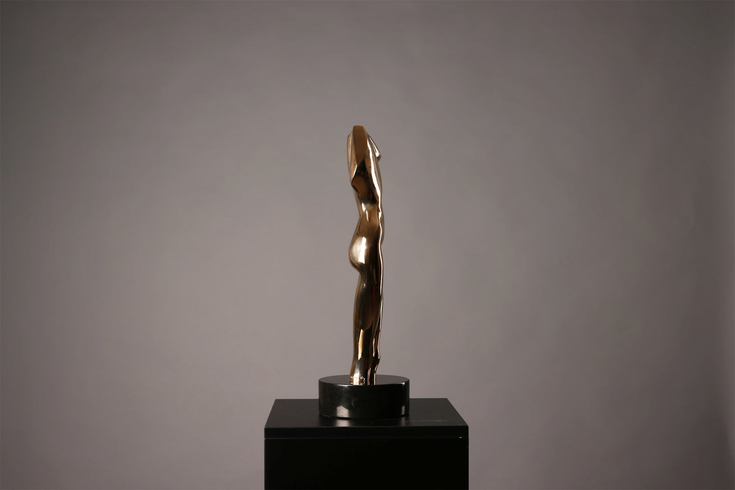 Bronze sculpture on a black pedestal against a gray background