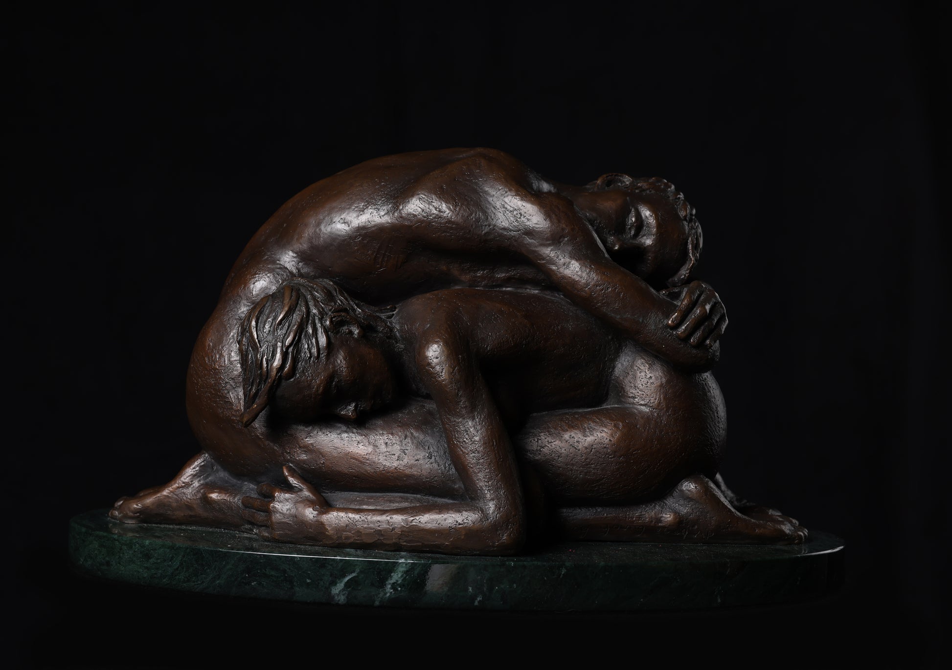 Bronze sculpture of two figures embracing on a dark background