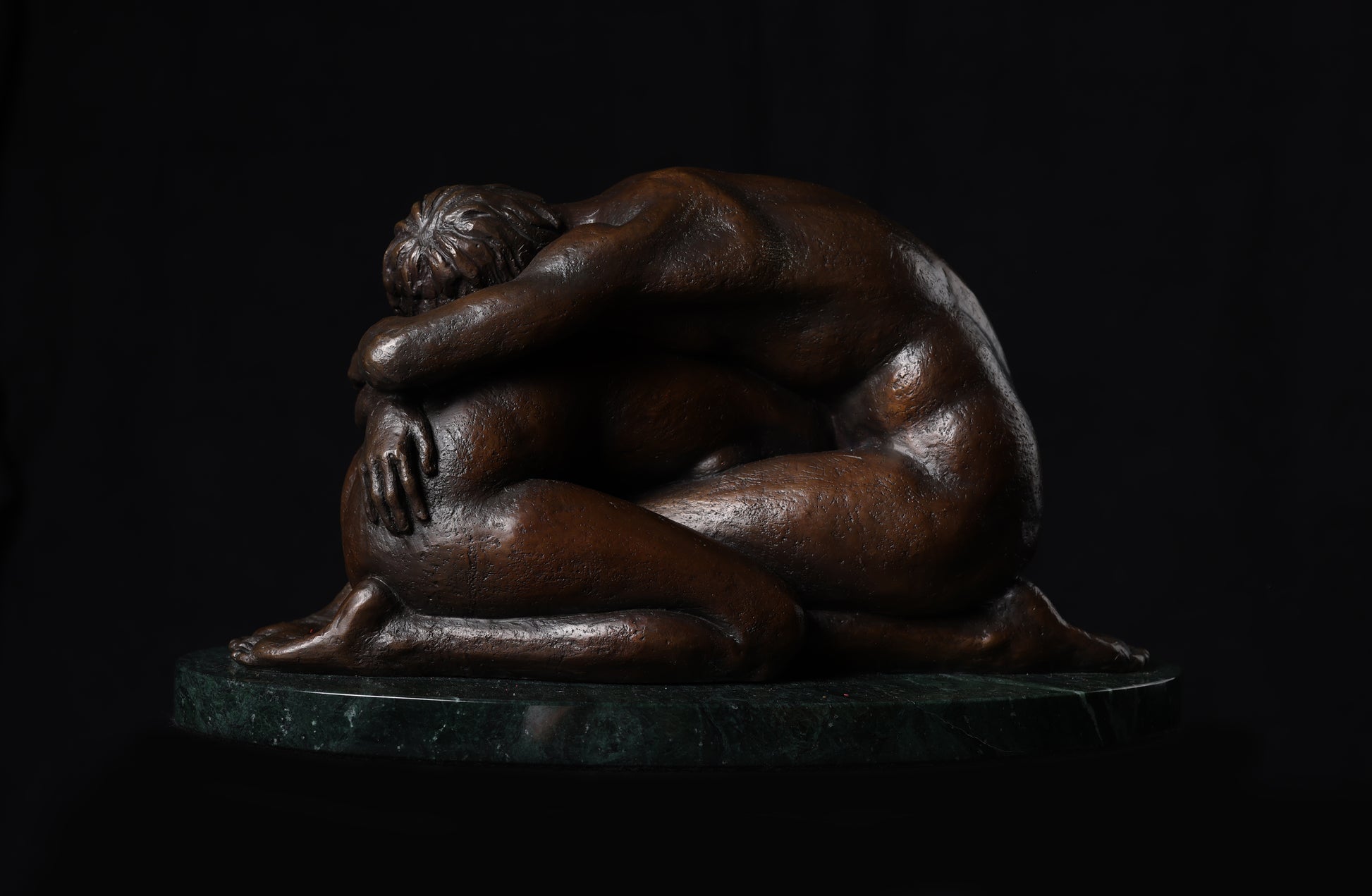 Bronze sculpture of two people embracing on a dark background