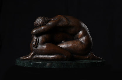 Bronze sculpture of two people embracing on a dark background