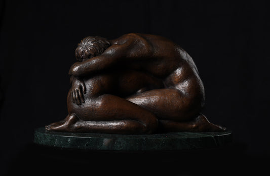 Bronze sculpture of two people embracing on a dark background