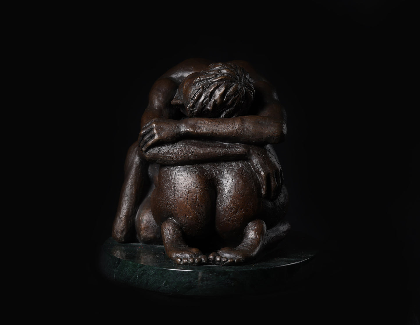 Bronze sculpture of a figure with arms wrapped around itself on a black background