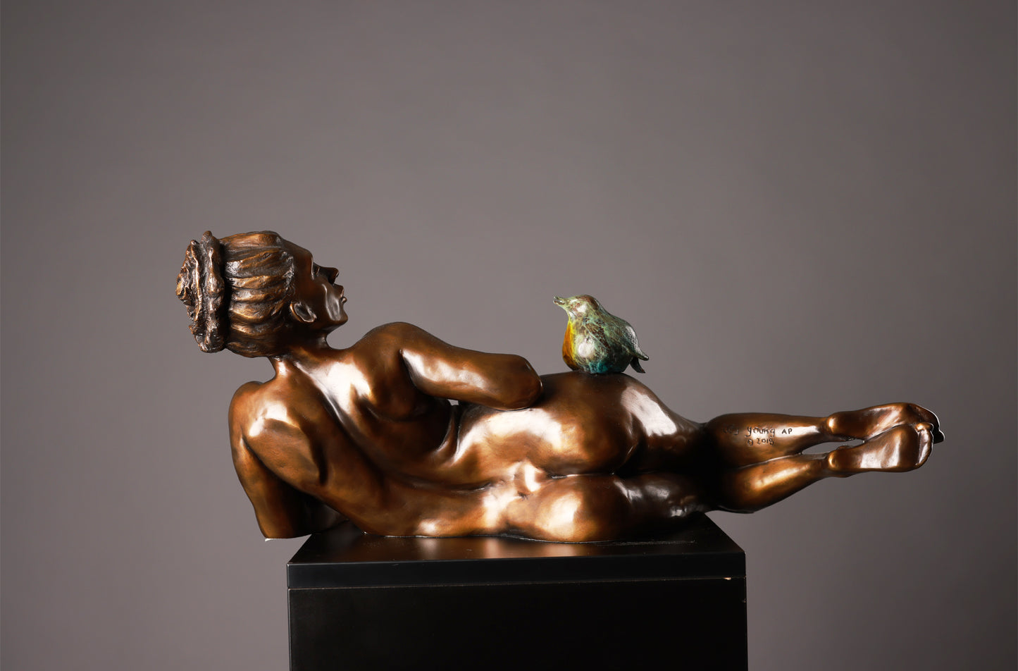 Bronze sculpture of a reclining figure with a bird on a gray background