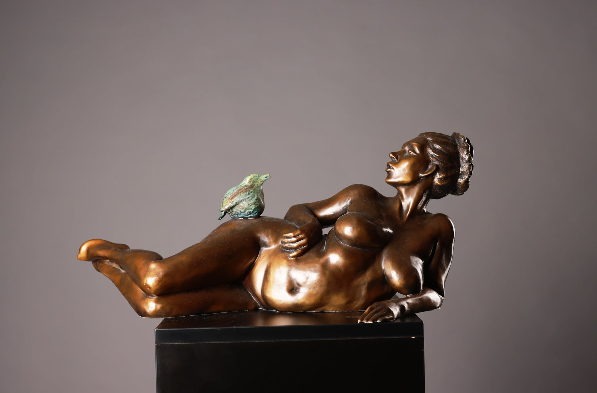 Bronze sculpture of a reclining woman with a bird on a gray background