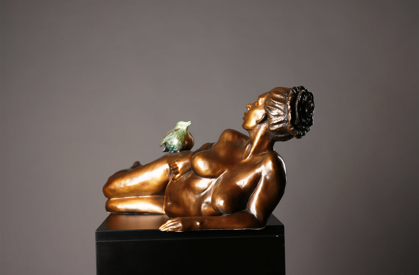 Bronze sculpture of a reclining figure with a bird on a gray background