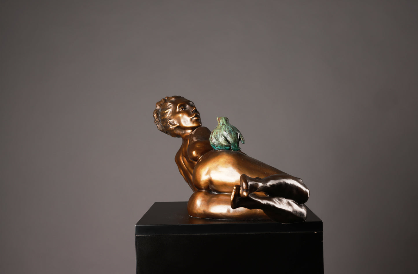 Bronze sculpture of a reclining figure with a green object on a black pedestal against a gray background