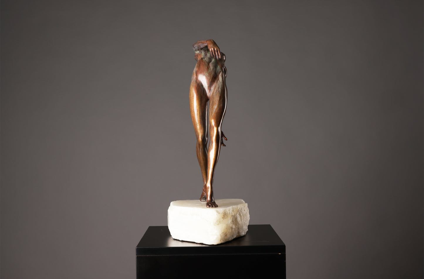 Bronze sculpture of a nude figure on a marble base against a gray background