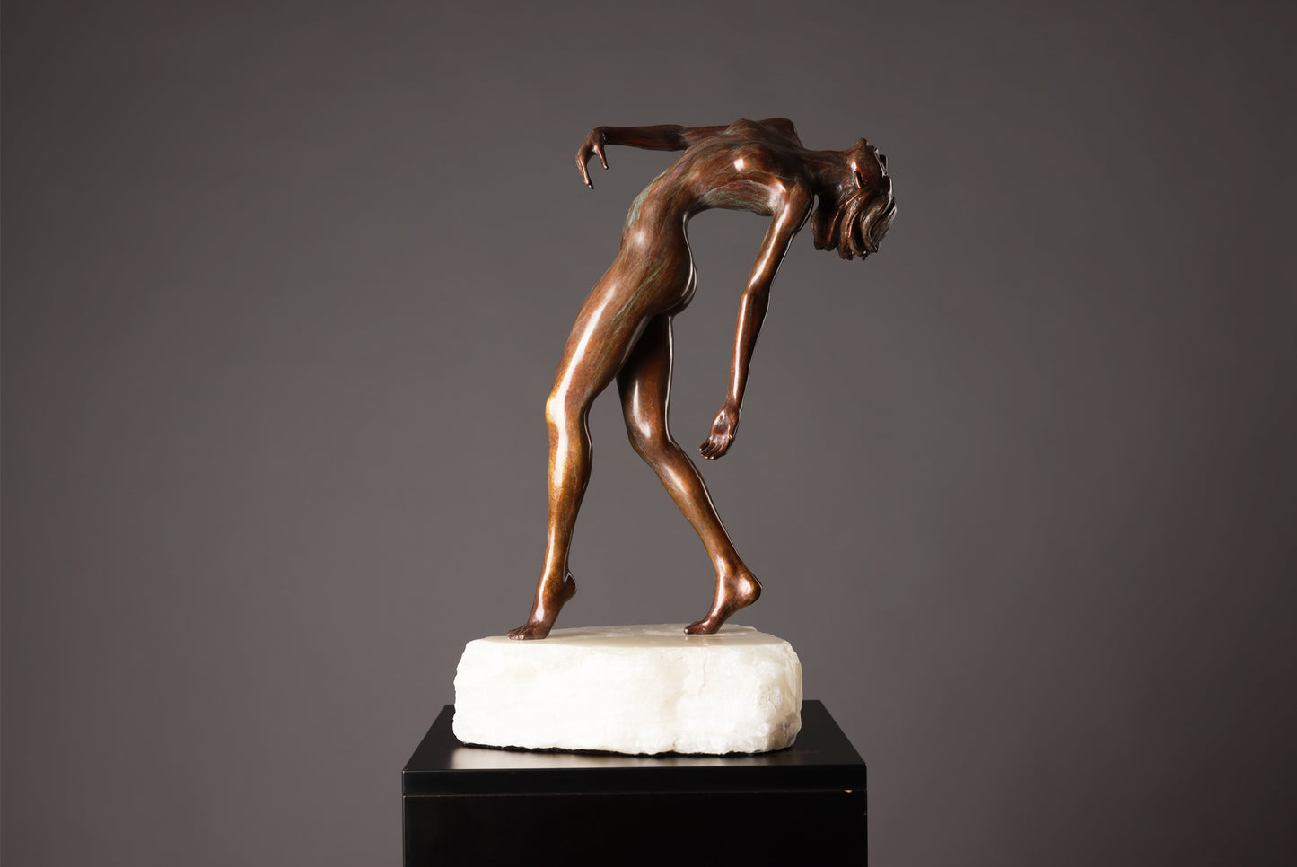 Bronze sculpture of a nude figure on a marble base against a gray background