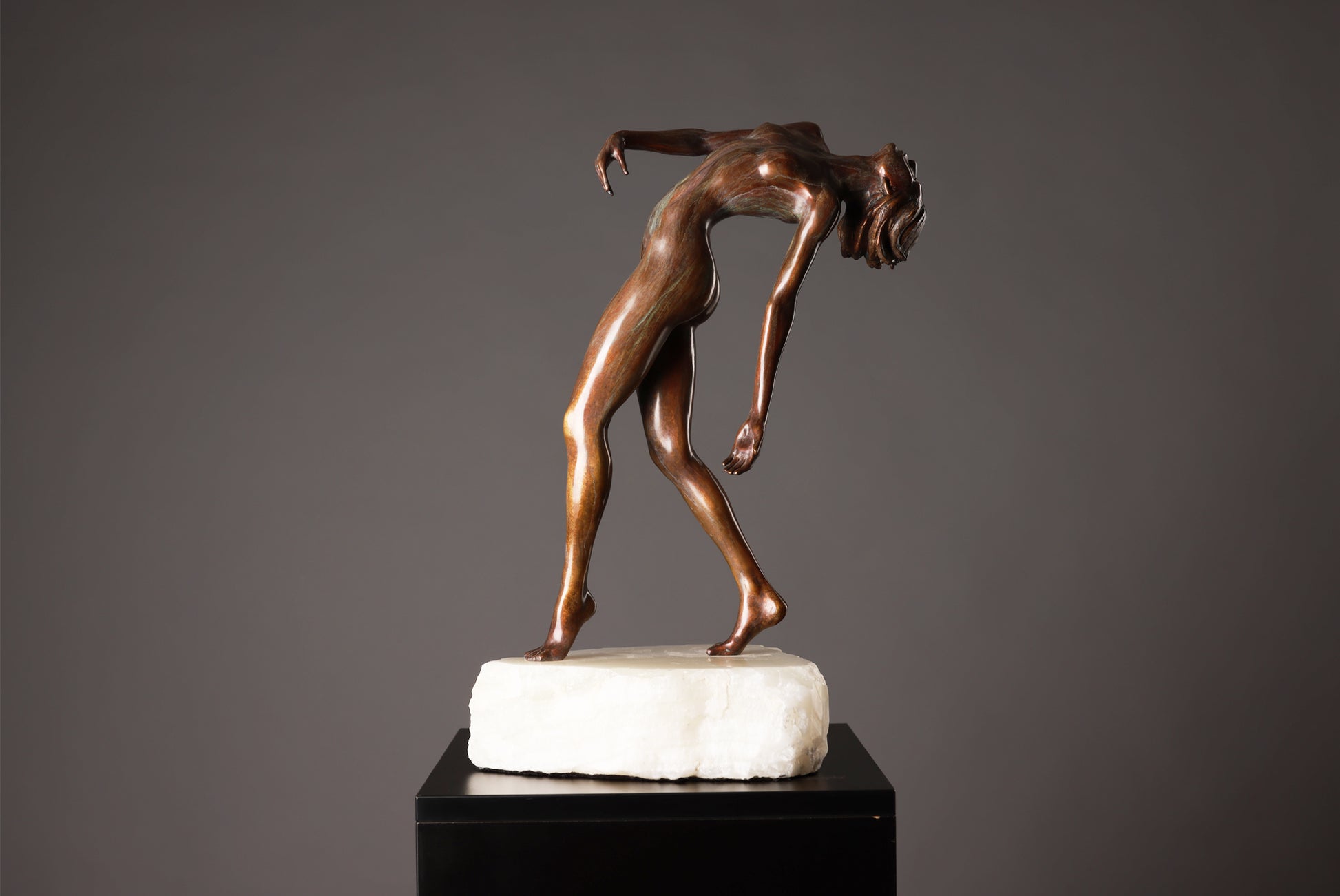 Bronze sculpture of a nude figure on a marble base against a gray background