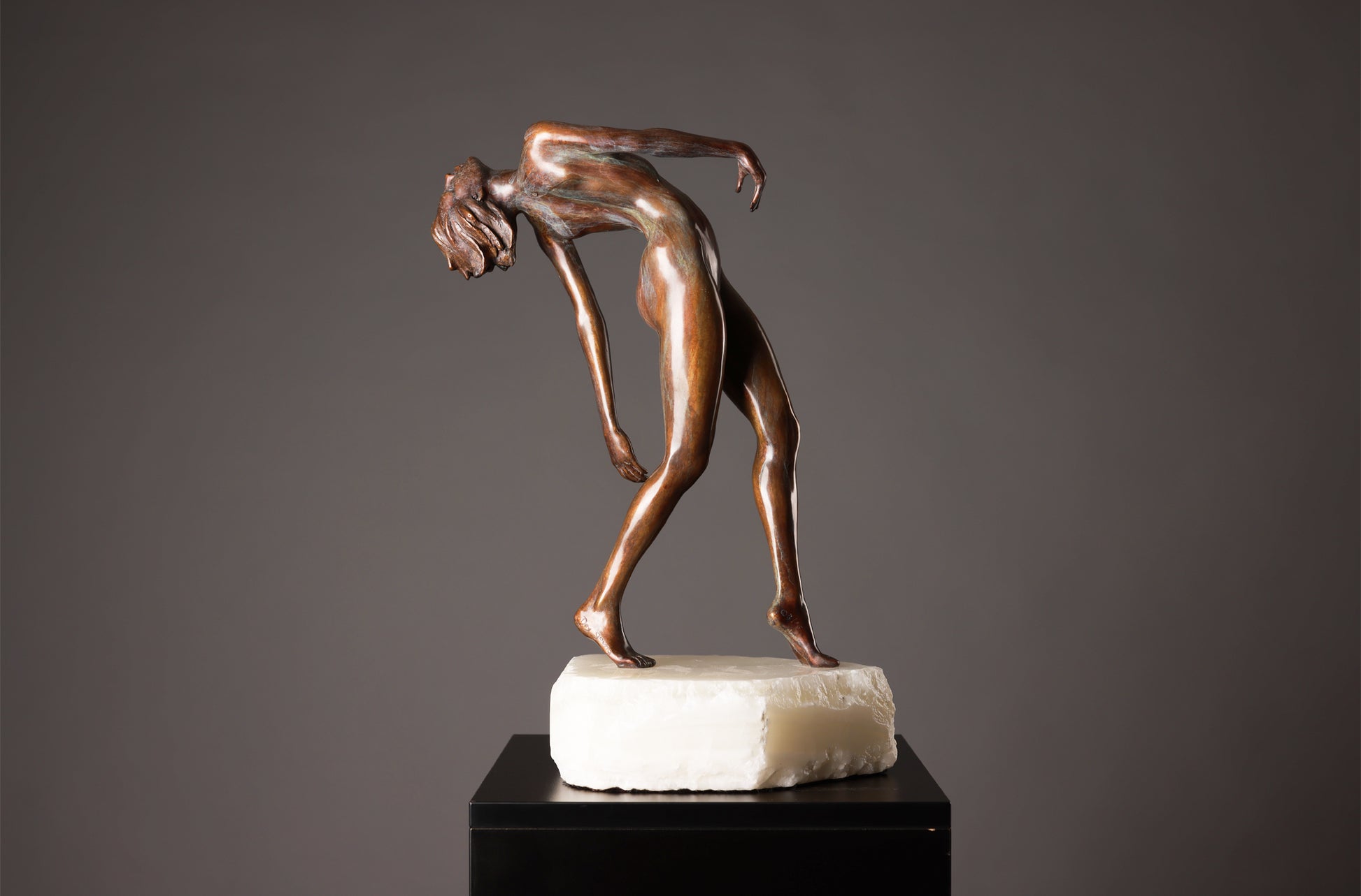 Bronze sculpture of a nude figure on a gray background