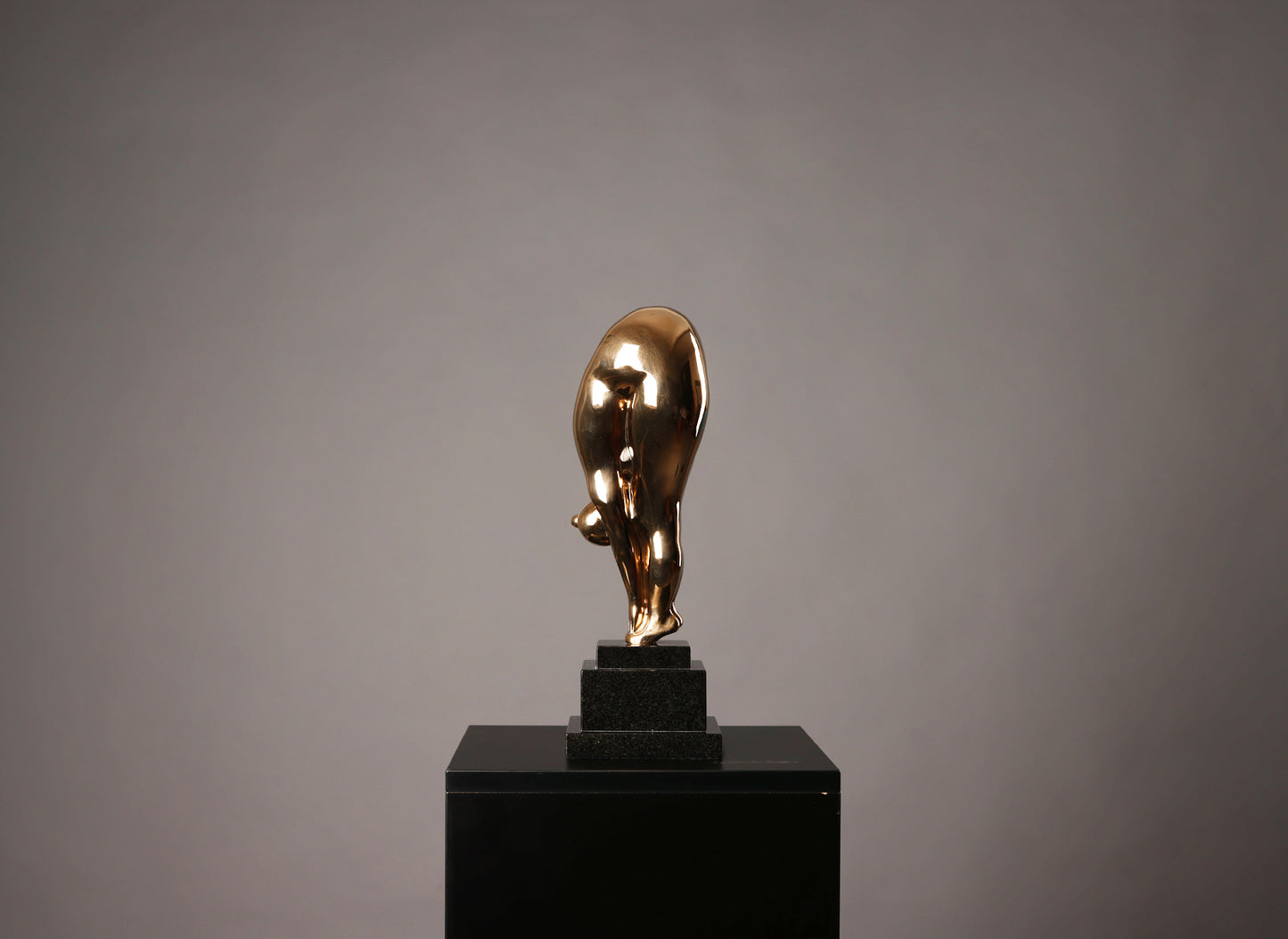 Gold bull statue on a black pedestal against a gray background