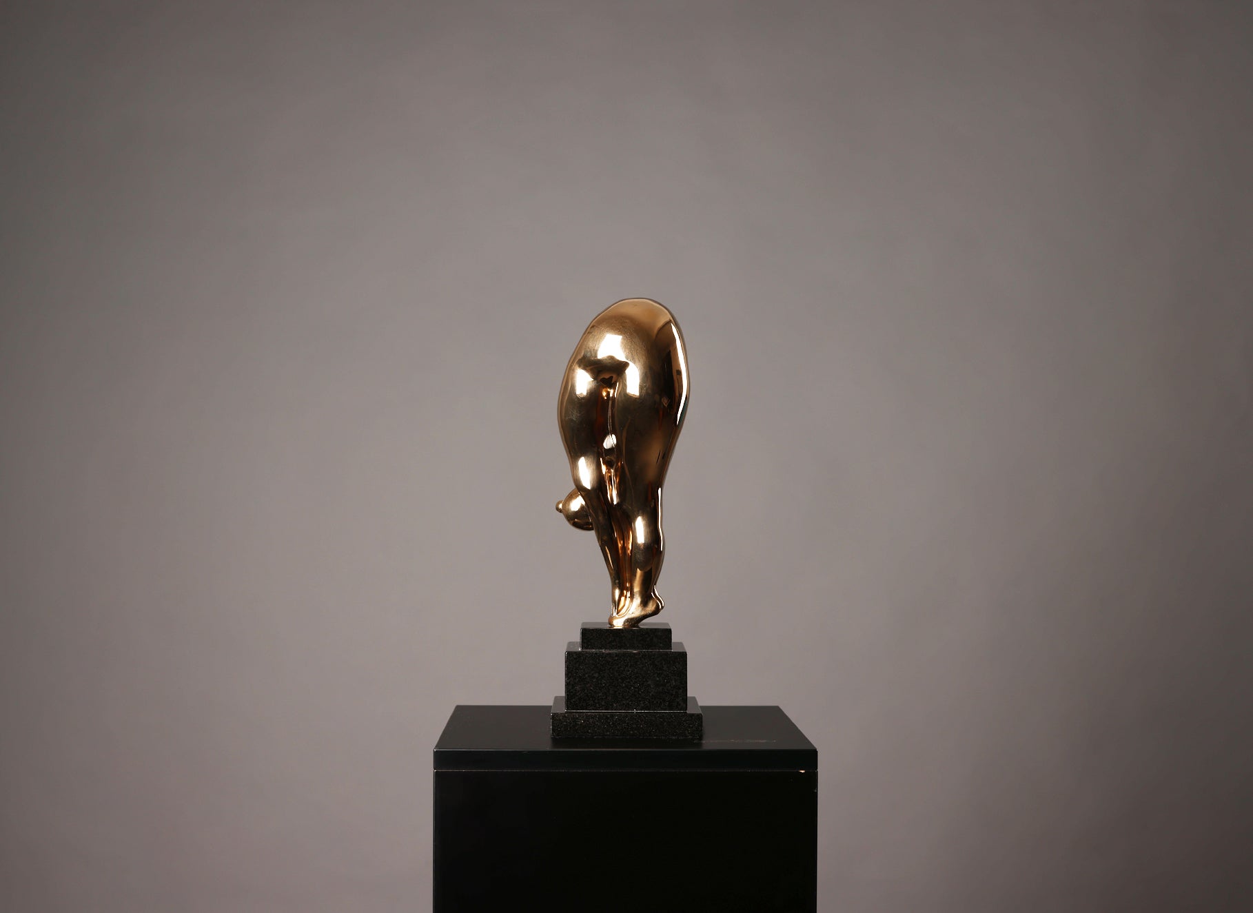 Gold bull statue on a black pedestal against a gray background
