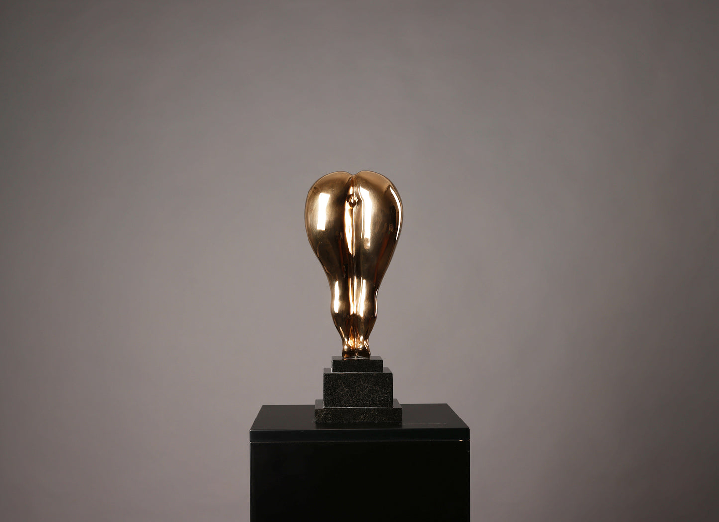Gold light bulb sculpture on a black pedestal against a gray background