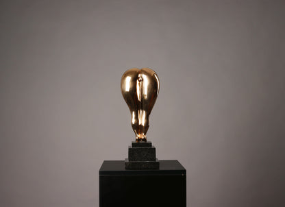 Gold light bulb sculpture on a black pedestal against a gray background