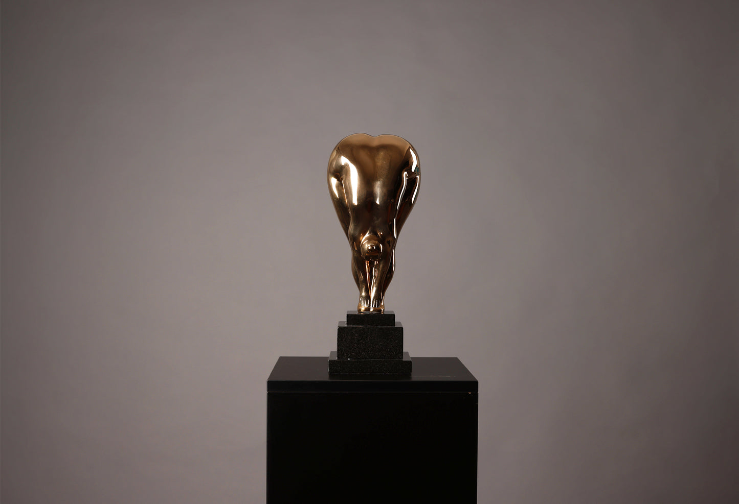Bronze sculpture of a bull on a black pedestal against a gray background