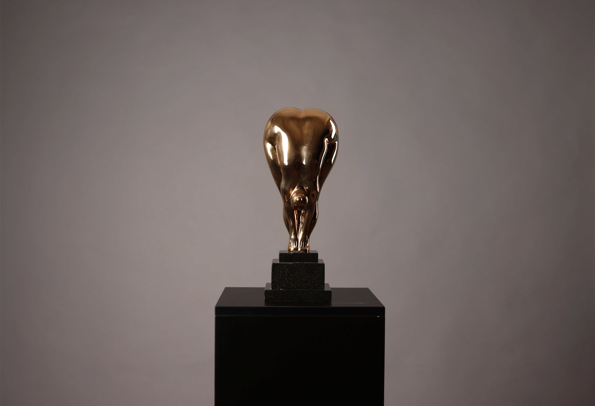 Bronze sculpture of a bull on a black pedestal against a gray background