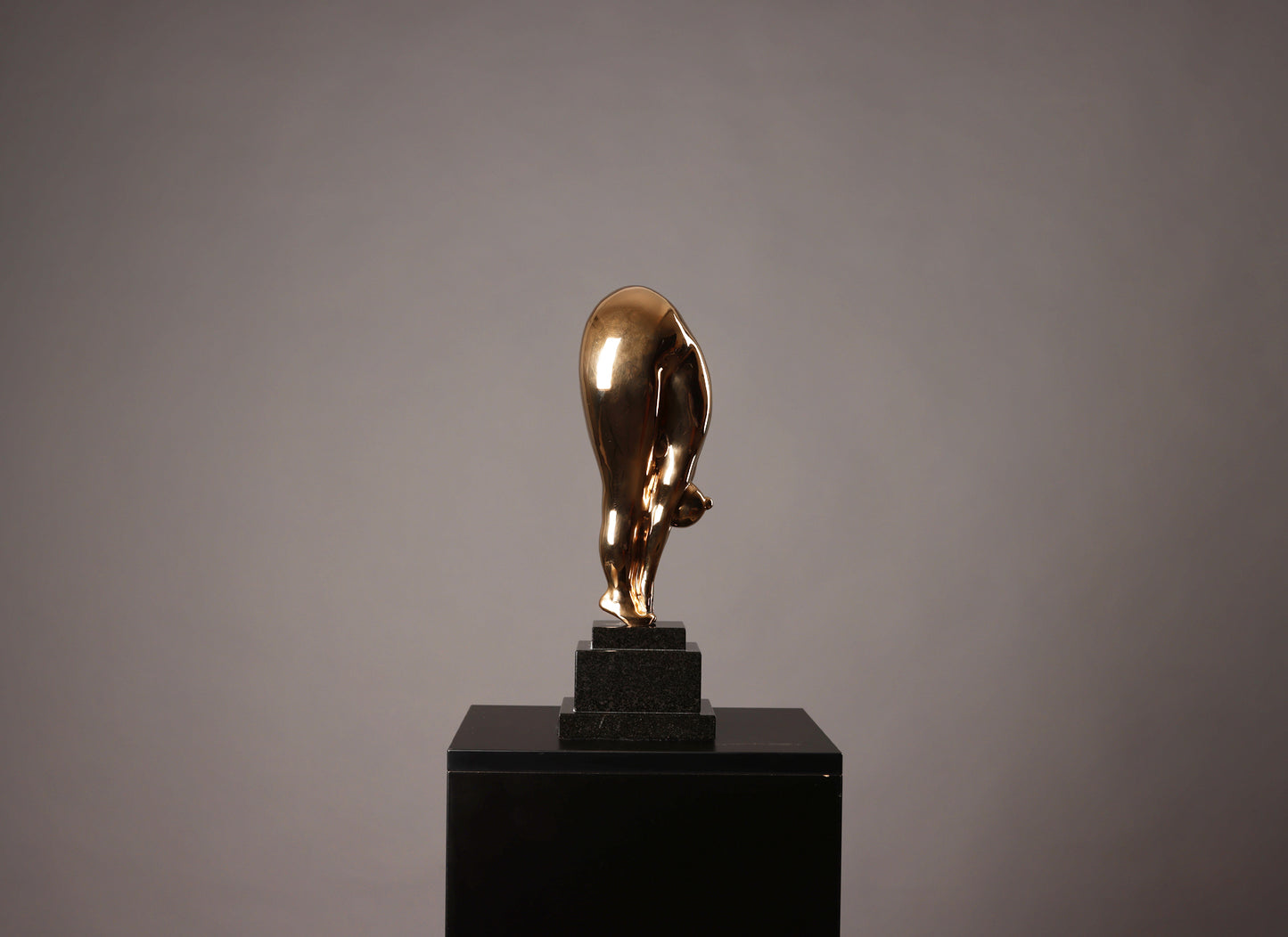 Gold bull statue on a black pedestal against a gray background
