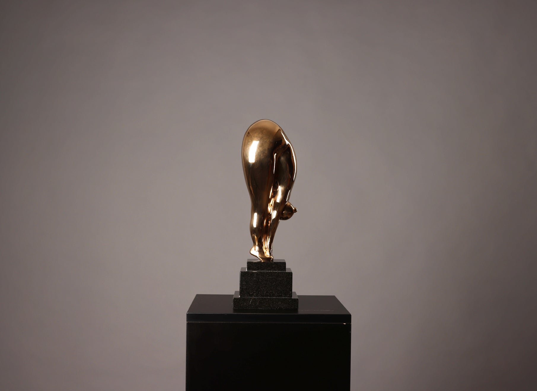 Gold bull statue on a black pedestal against a gray background