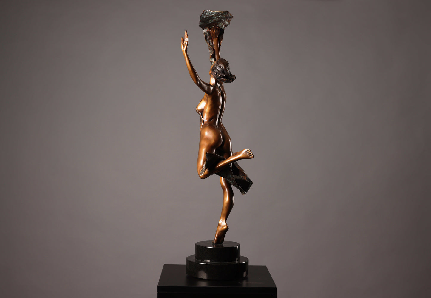 Bronze sculpture of a dancer holding a rock on a gray background