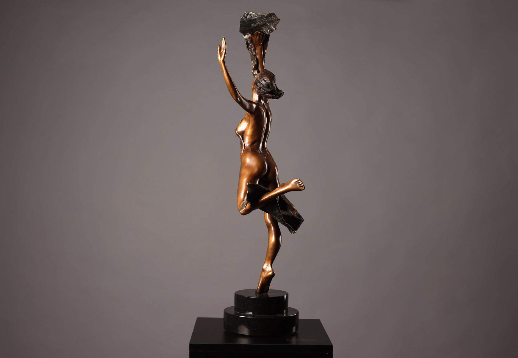 Bronze sculpture of a dancer holding a rock on a gray background