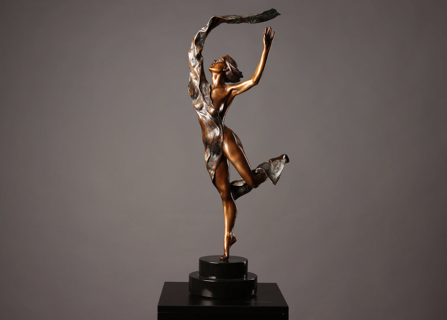 Bronze sculpture of a dancer on a black base against a gray background