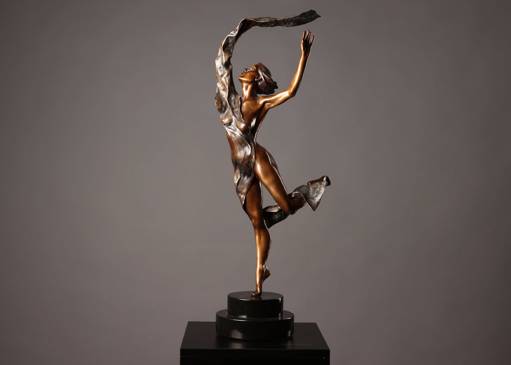 Bronze sculpture of a dancer on a black base against a gray background