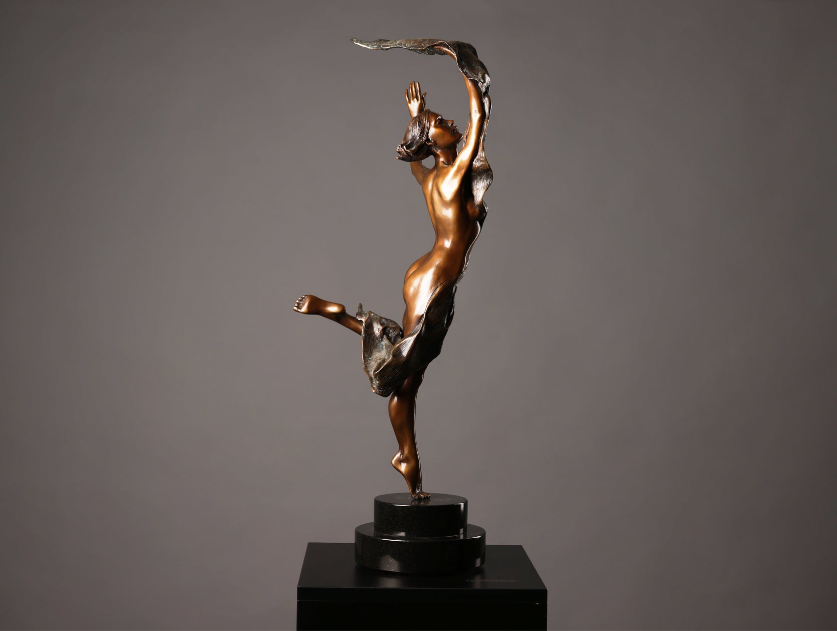 Bronze sculpture of a dancer on a black base against a gray background