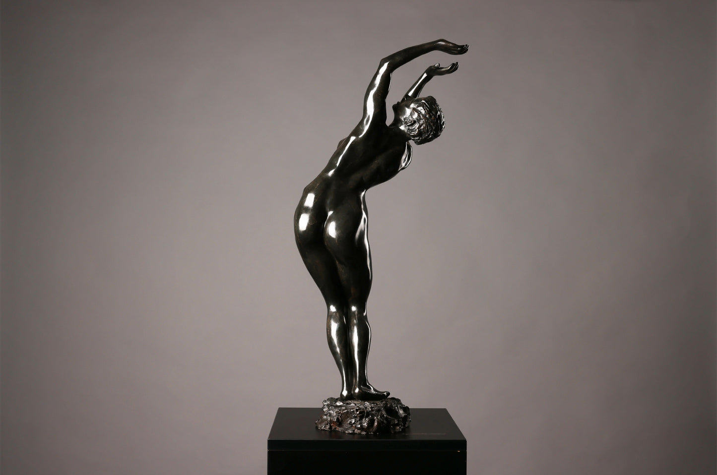 Statue of a nude figure on a pedestal against a gray background