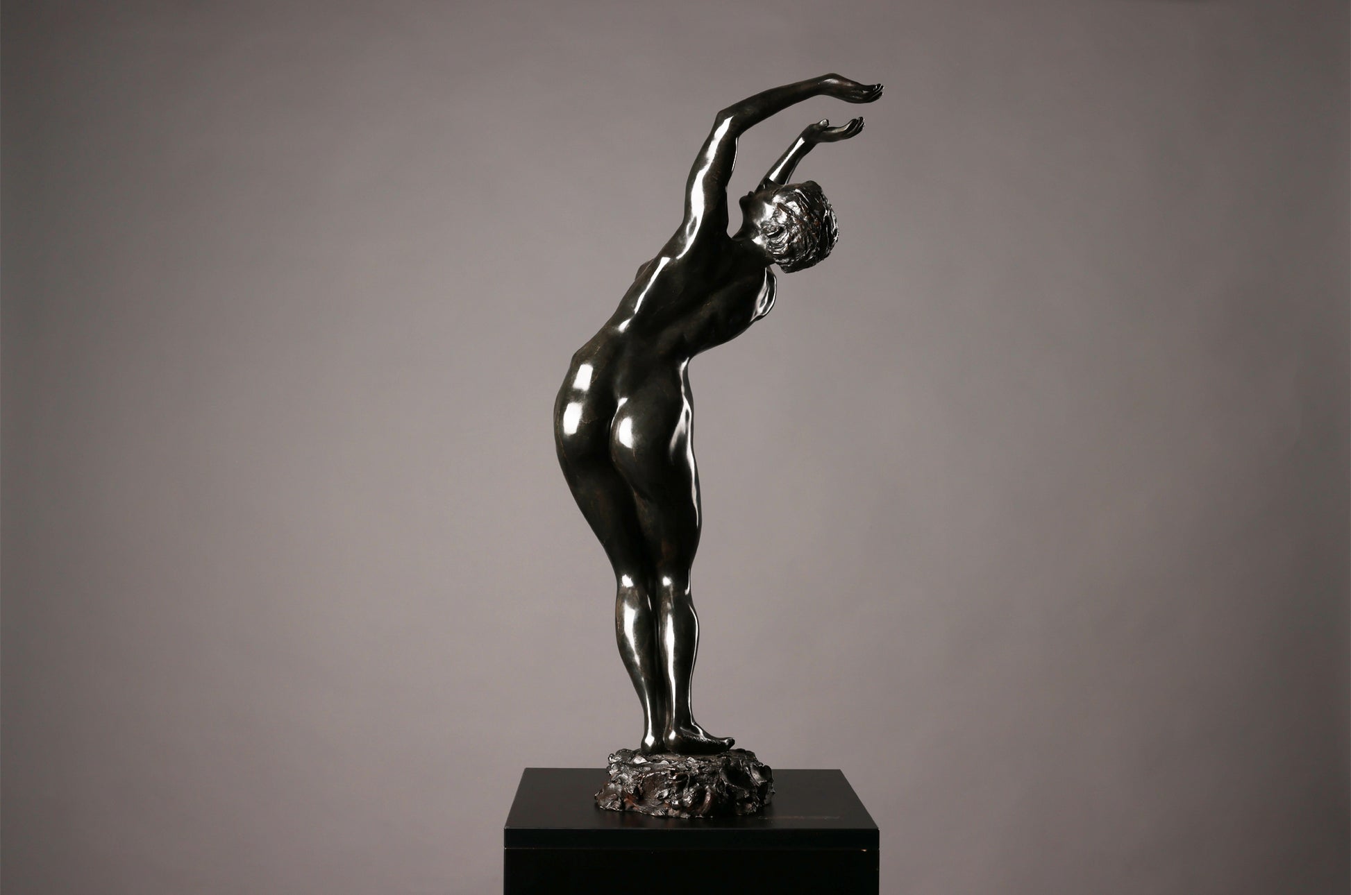 Statue of a nude figure on a pedestal against a gray background