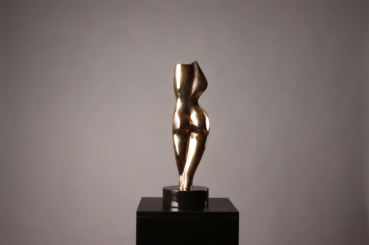 Bronze sculpture of a female figure on a black pedestal against a gray background
