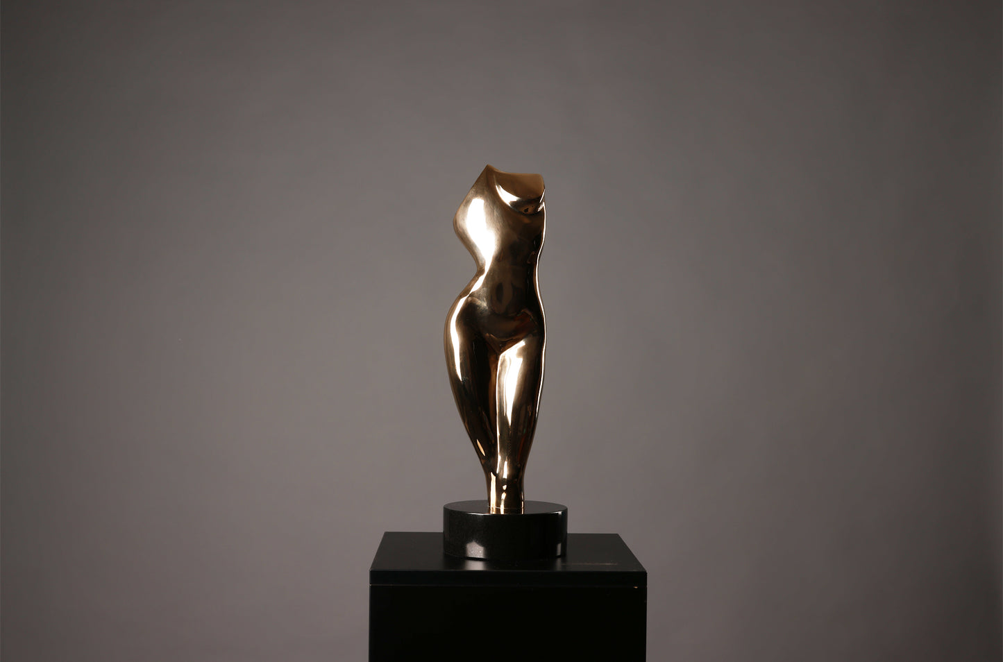 Bronze sculpture of a nude figure on a black pedestal against a gray background