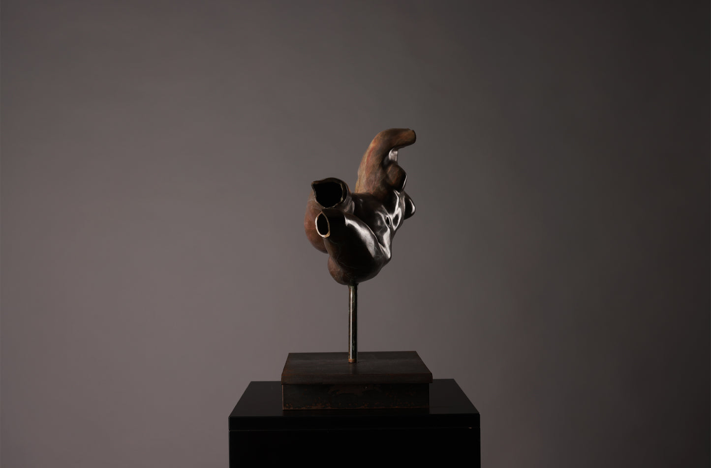 Abstract sculpture on a dark pedestal against a gray background