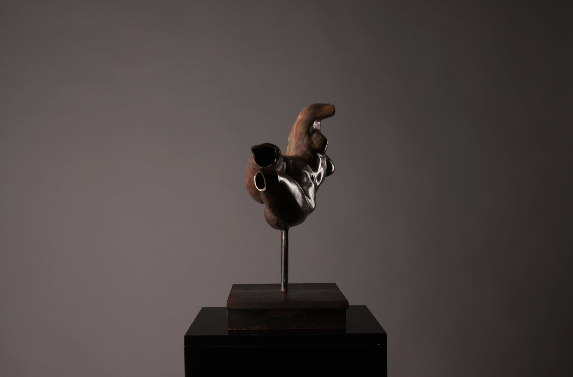 Abstract sculpture on a dark pedestal against a gray background