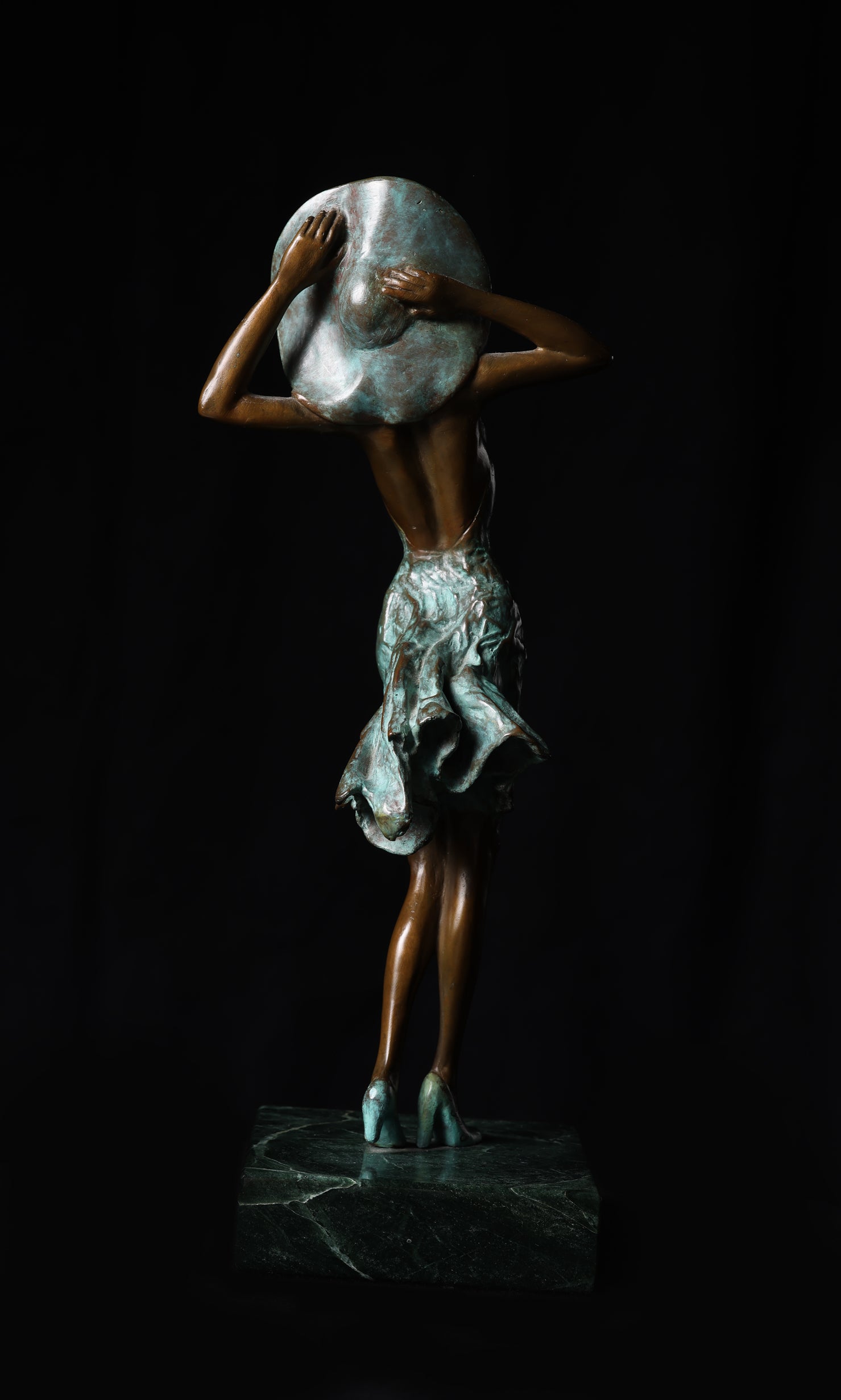 Bronze sculpture of a figure holding a large moon-like object against a black background